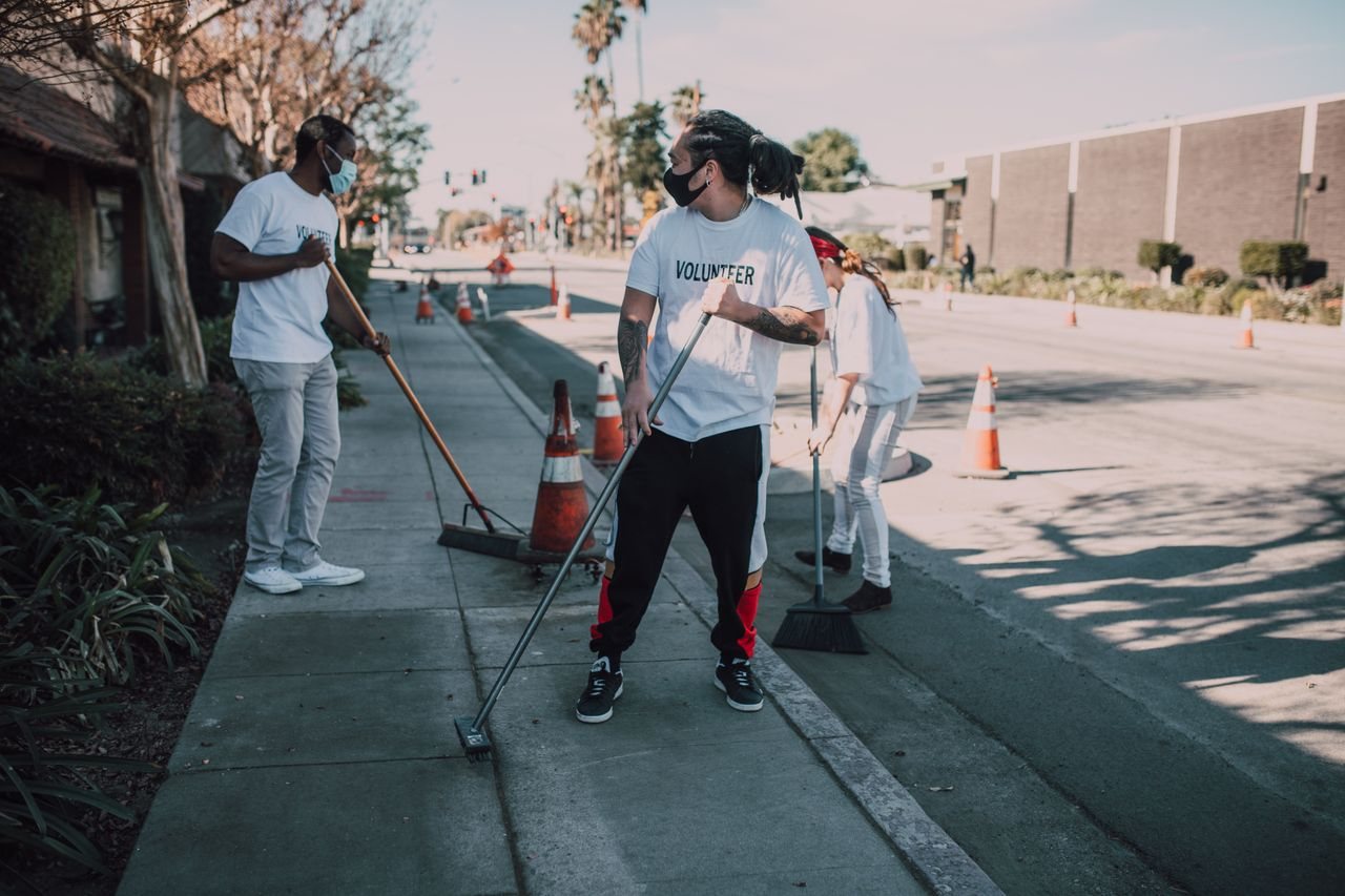 Free Volunteers wearing masks sweep an urban sidewalk, enhancing community and social good efforts. Stock Photo