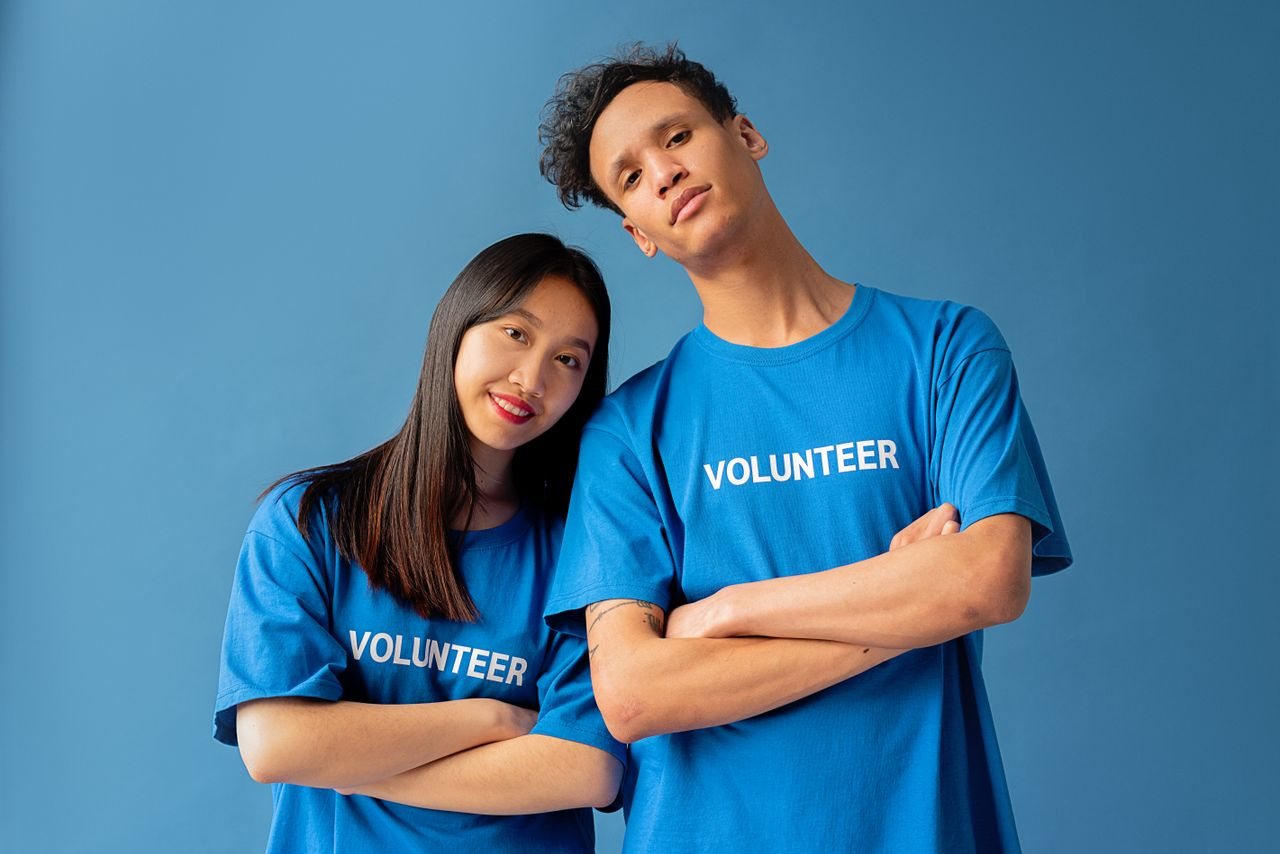 Free Two young volunteers in blue shirts pose confidently against a blue backdrop. Stock Photo